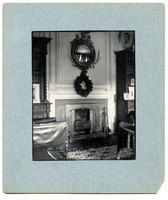 Black and white photograph of wreath hanging over fire place in 19th century study.