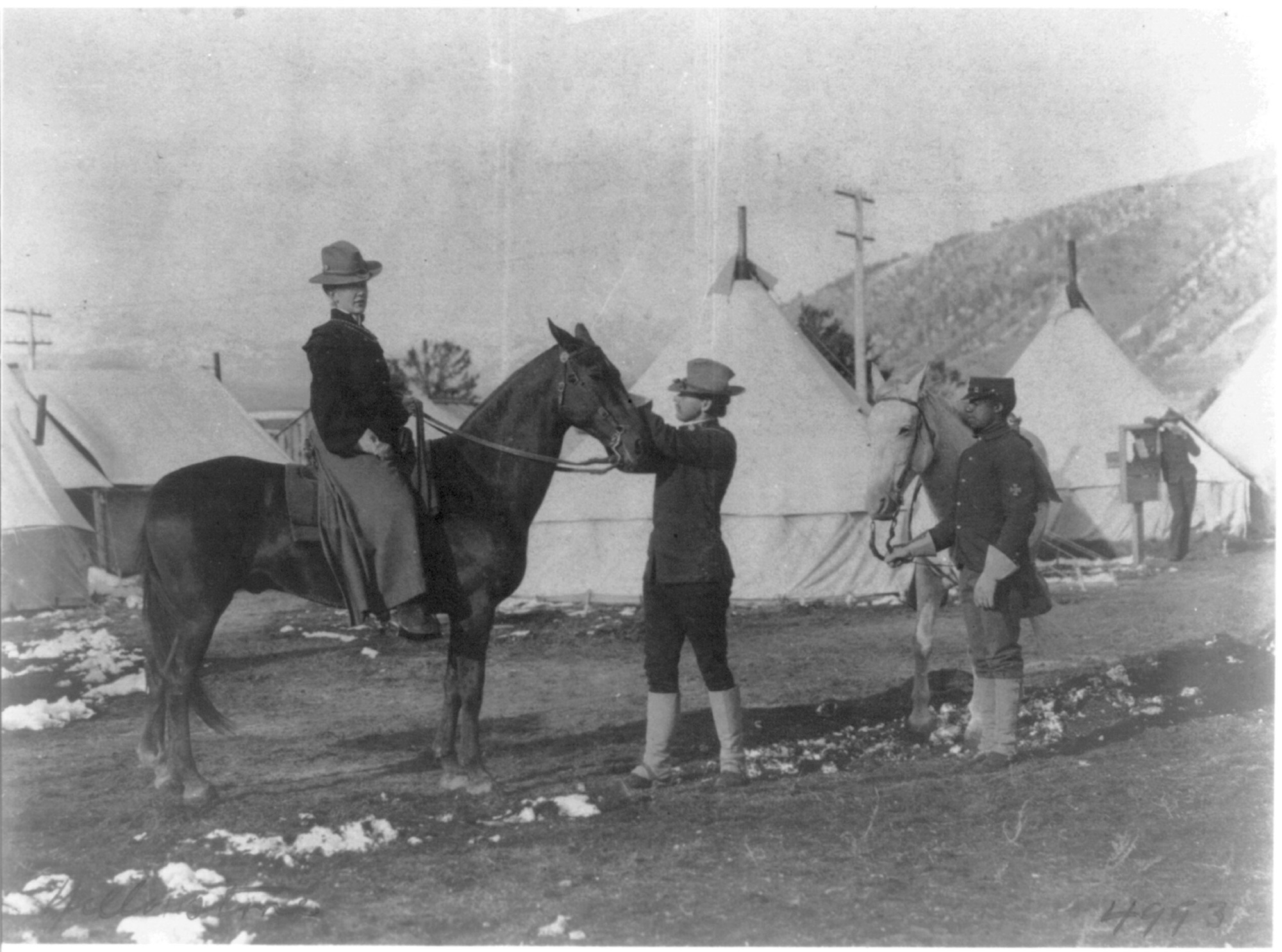 (U.S. soldier-guide holding woman's horse, African American trooper alongside, tents in background, Yellowstone Park, Wyo.)