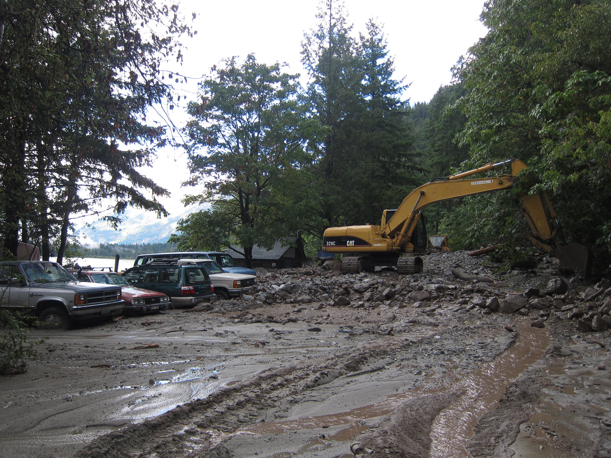 A yellow backhoe removes debris from a mudslide along a forested road