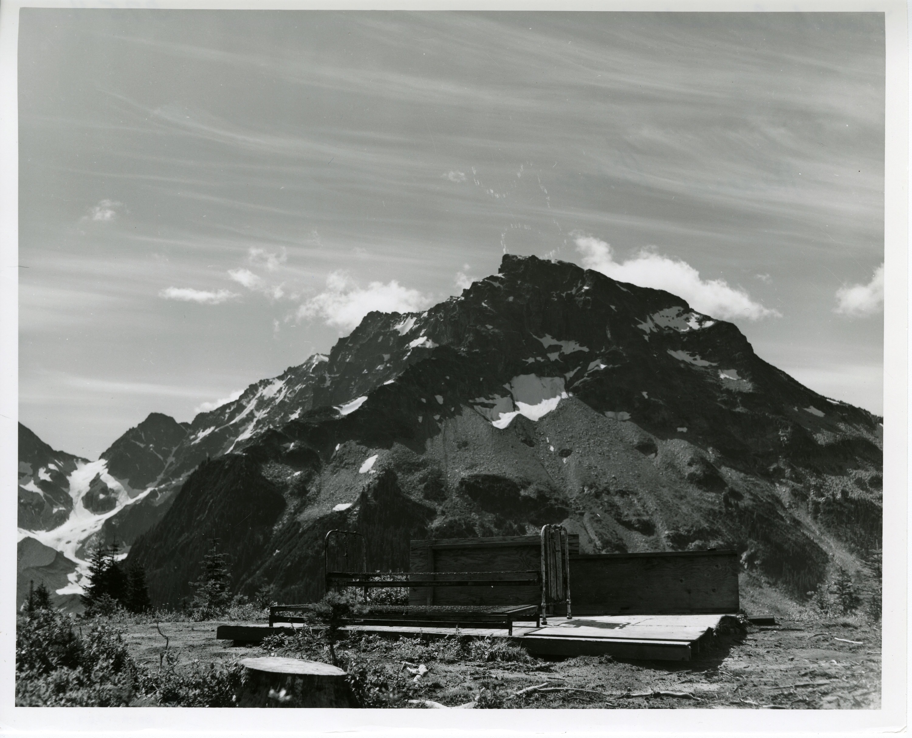 A wooden platform with a metal bedframe in the foreground, a mountain in the background.