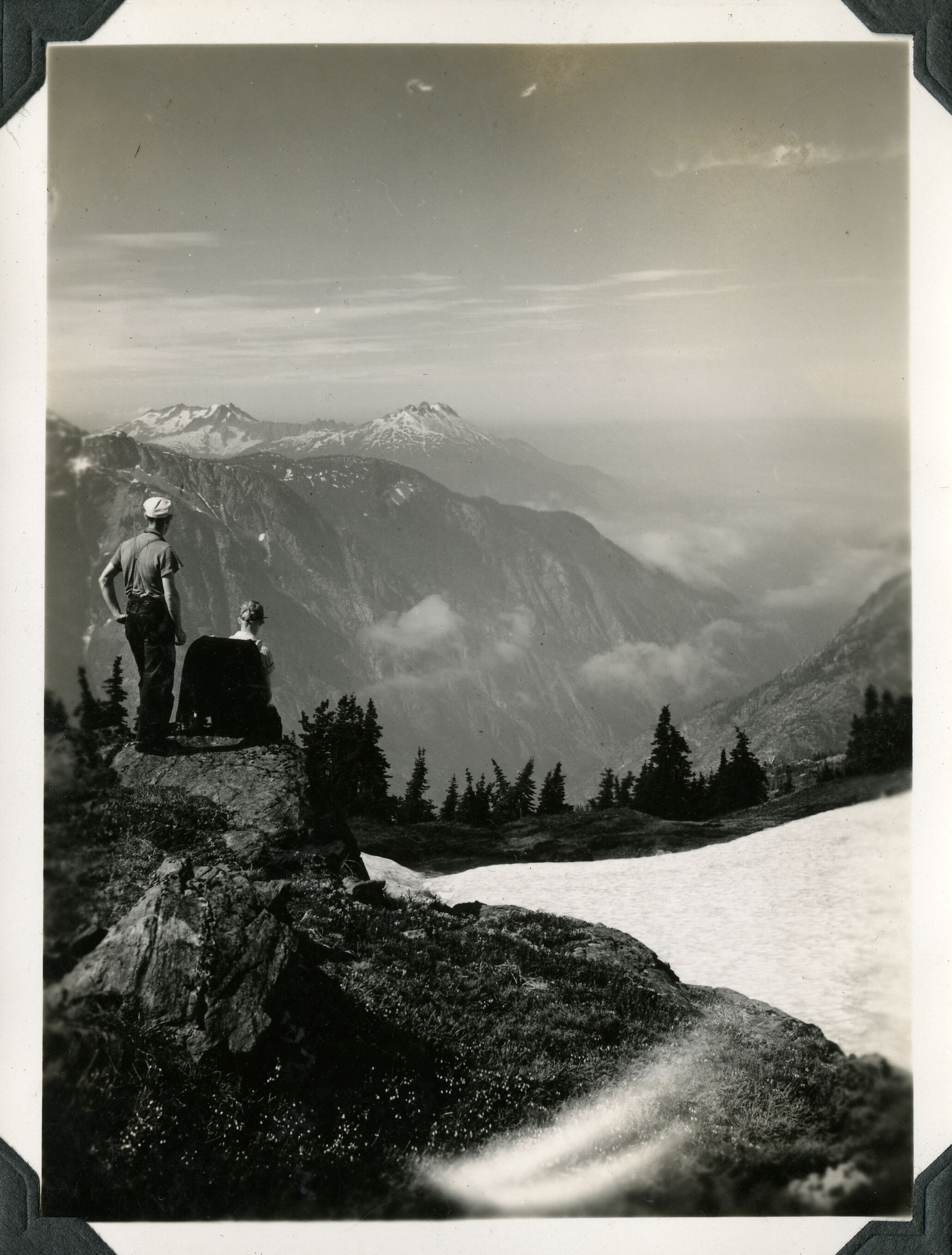 Two people sitting on a boulder looking toward mountain peaks in the distance.