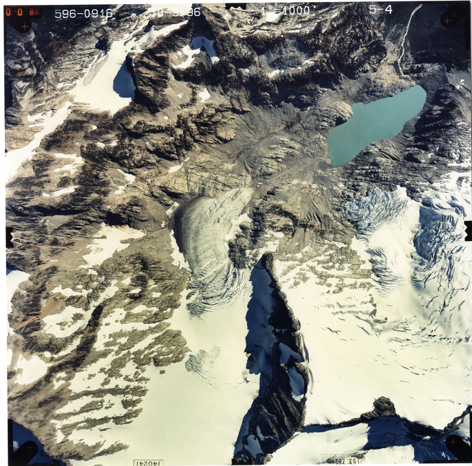 Color aerial photograph of glacier, snowfields, and alpine lake on mountain peak.