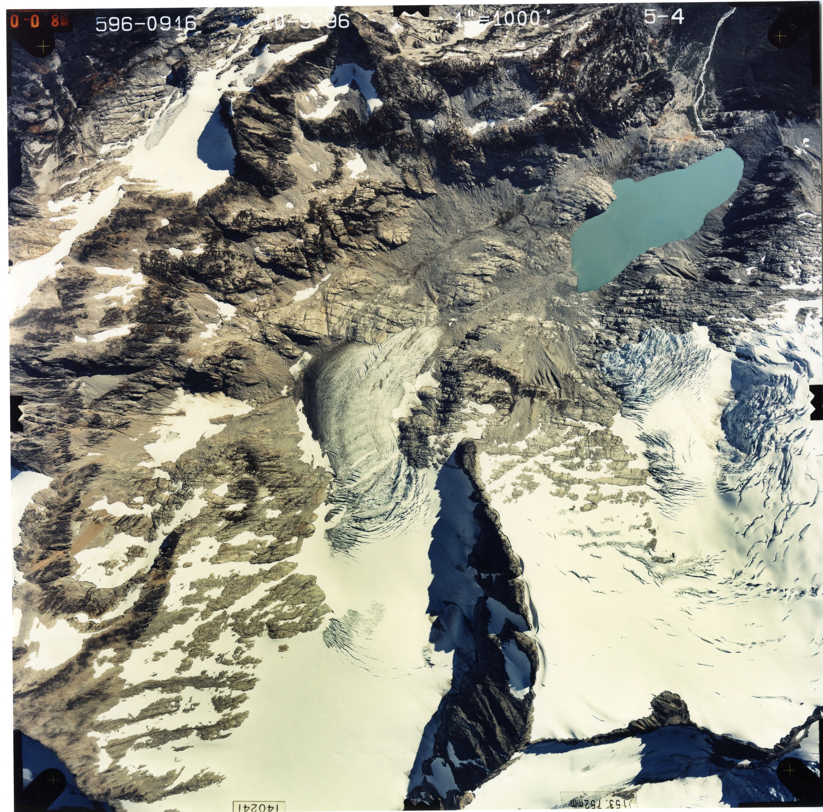 Color aerial photograph of glacier, snowfields, and alpine lake on mountain peak.