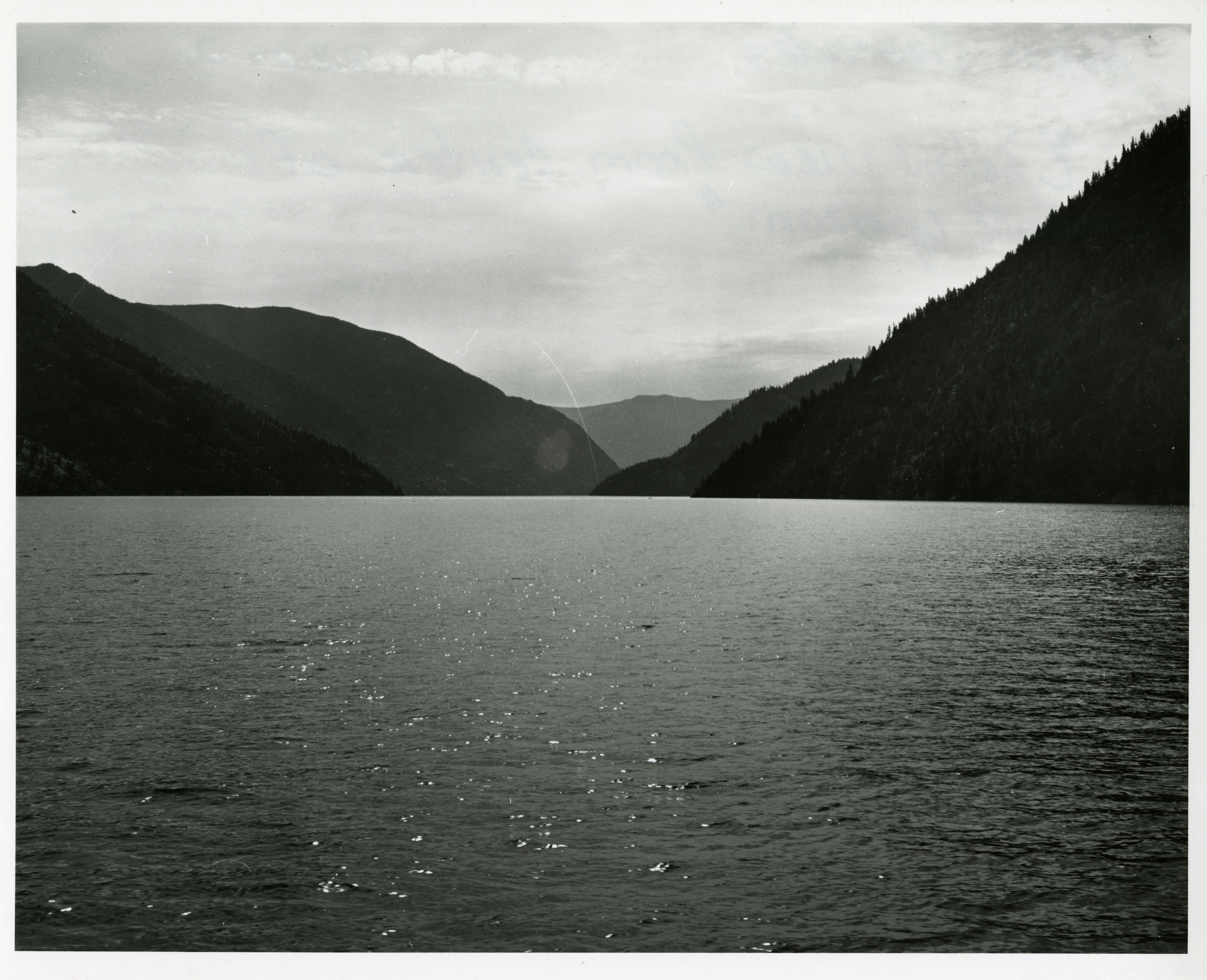 A rippled lake with forested ridges in the distance.