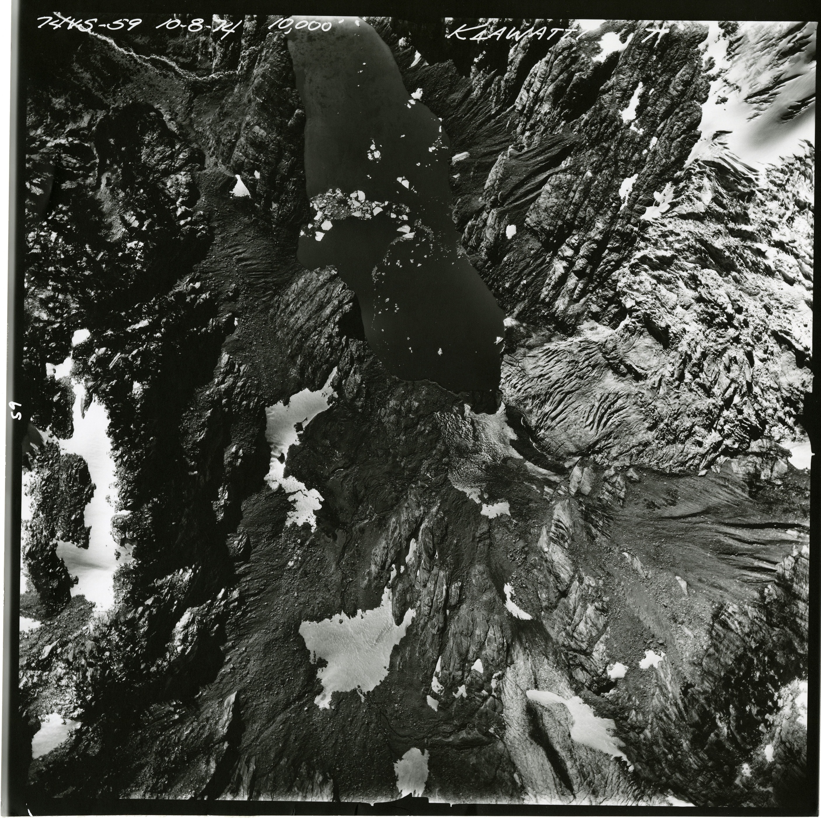 Black and white aerial photograph of glacier and alpine lake on mountain peak.