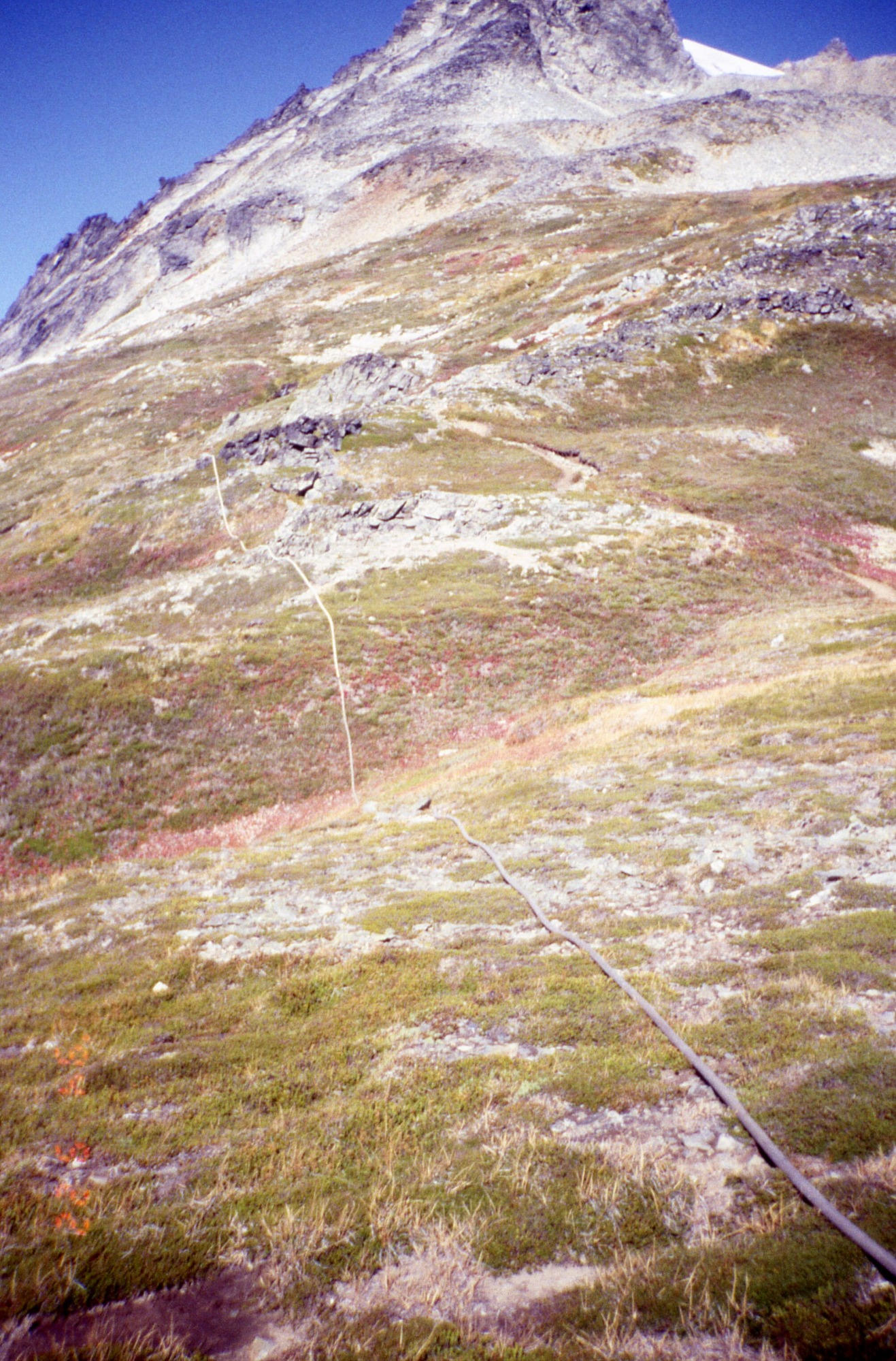 A water hose running down the side of a rocky hill. Above the hill is a snowy mountainside;