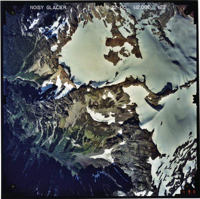 Color aerial photograph of glacier on mountain peak, surrounded by forested valleys.