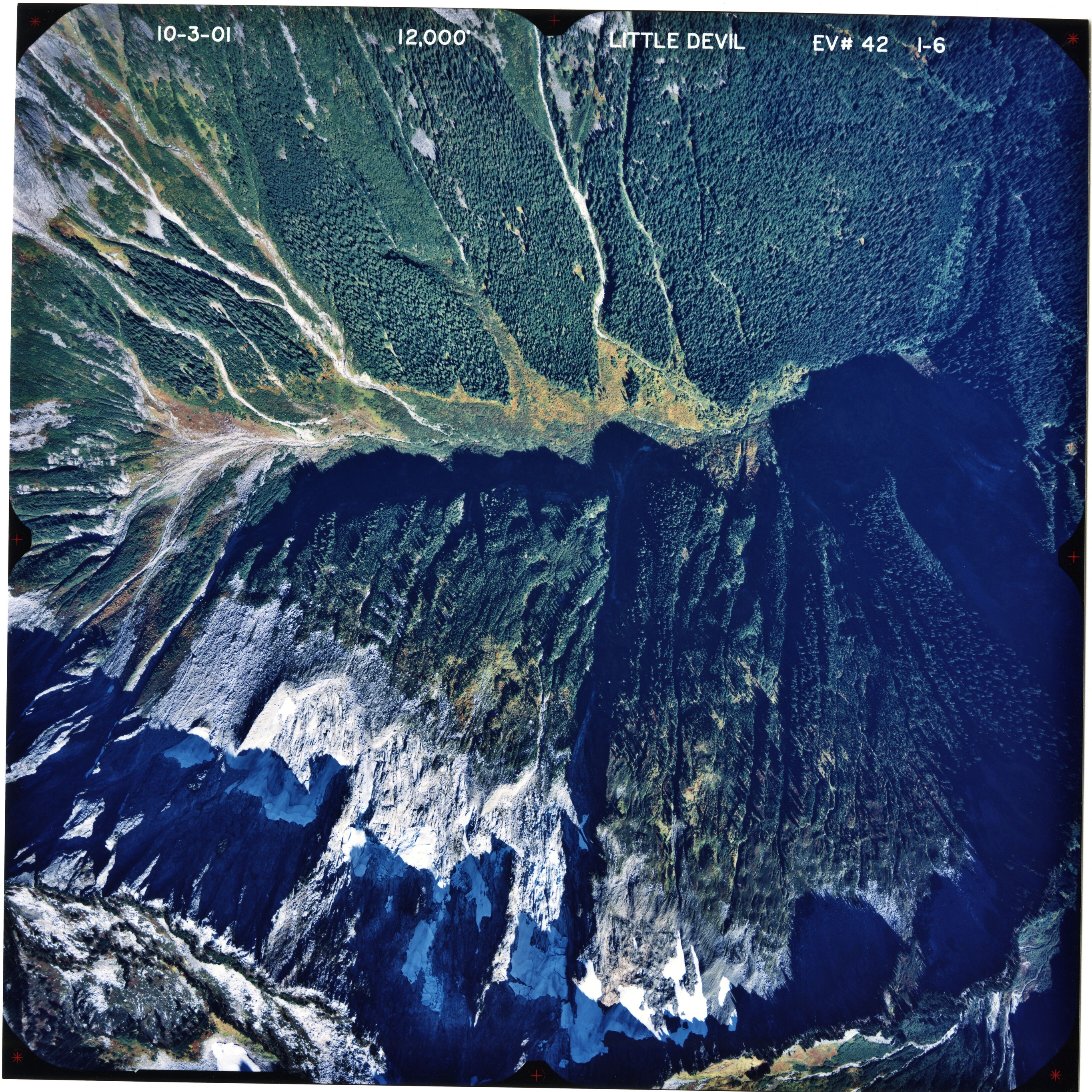 Color aerial photograph of glaciated mountain peak with forested valleys below.