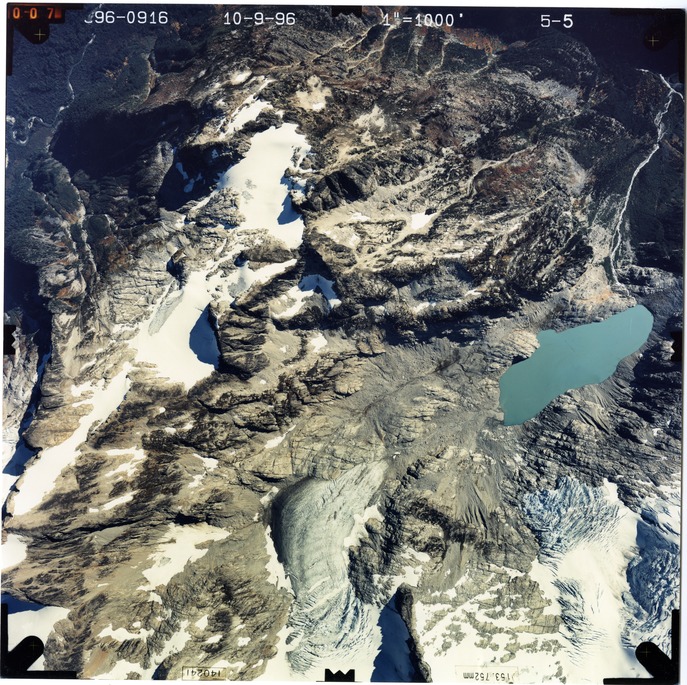 Color aerial photograph of glacier, snowfields, and alpine lake on mountain peak.