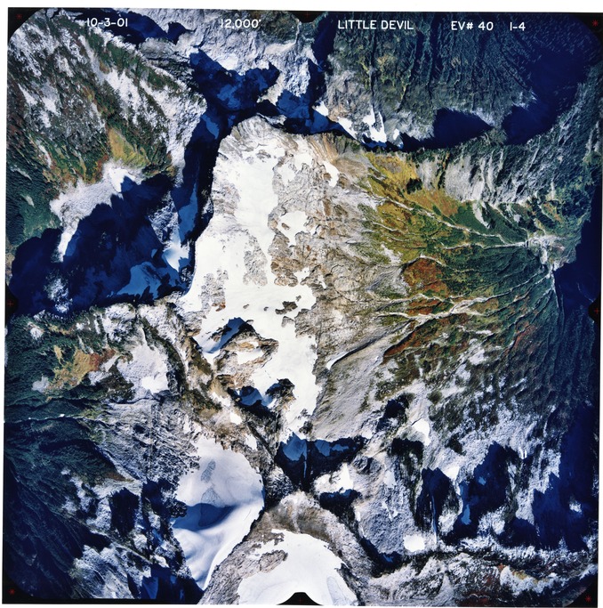 Color aerial photograph of glaciated mountain peak with forested valleys below.