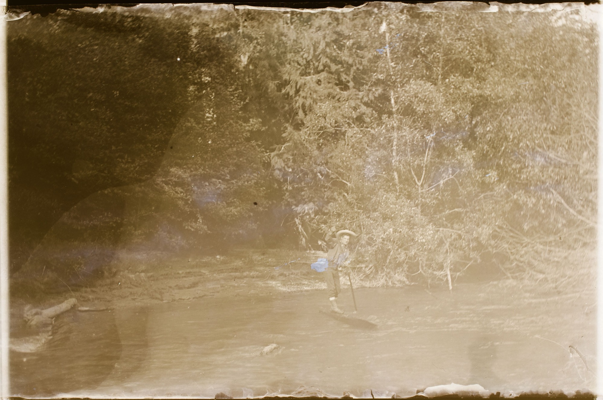 Man standing on log in water, using a pole to push himself.