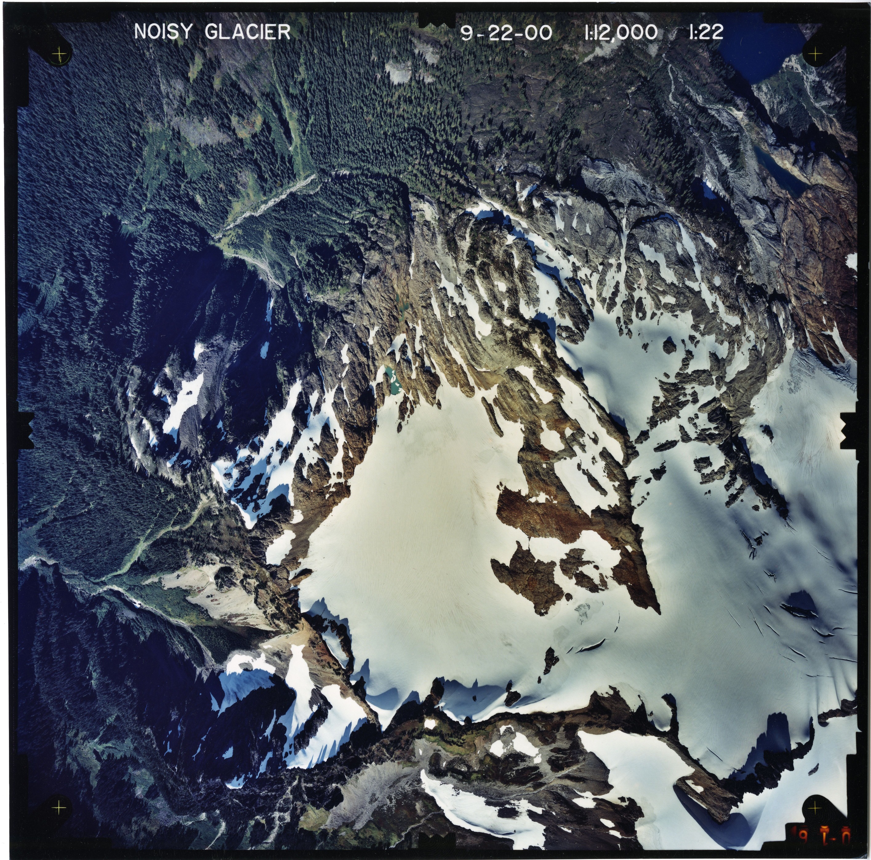 Color aerial photograph of glacier on mountain peak, surrounded by forested valleys.