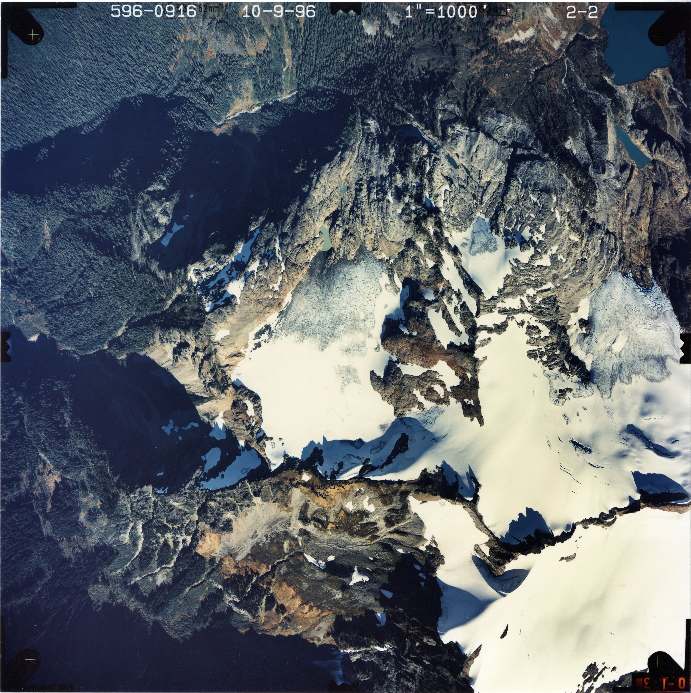 Color aerial photograph of glacier on mountain peak, surrounded by forested valleys.
