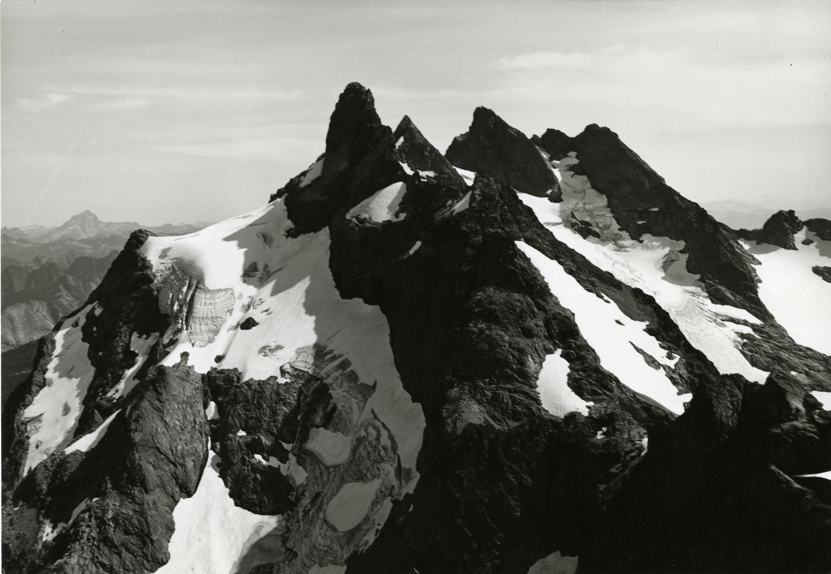 Rocky mountain peak with glacier and snow patches. More mountains can be seen in the background.