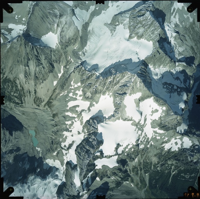 Color aerial photograph of glacier on mountain peak, surrounded by forested valleys.