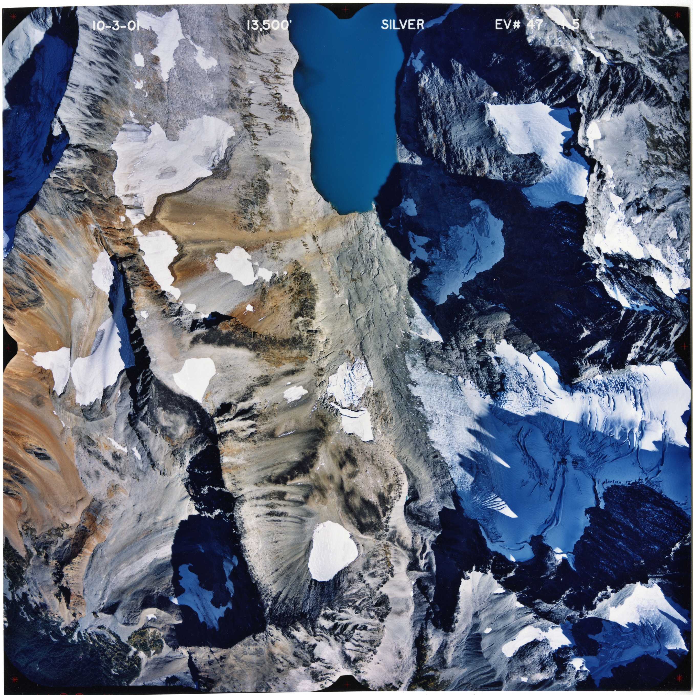 Color aerial photograph of glacier, snowfields and alpine lake on mountain peak.