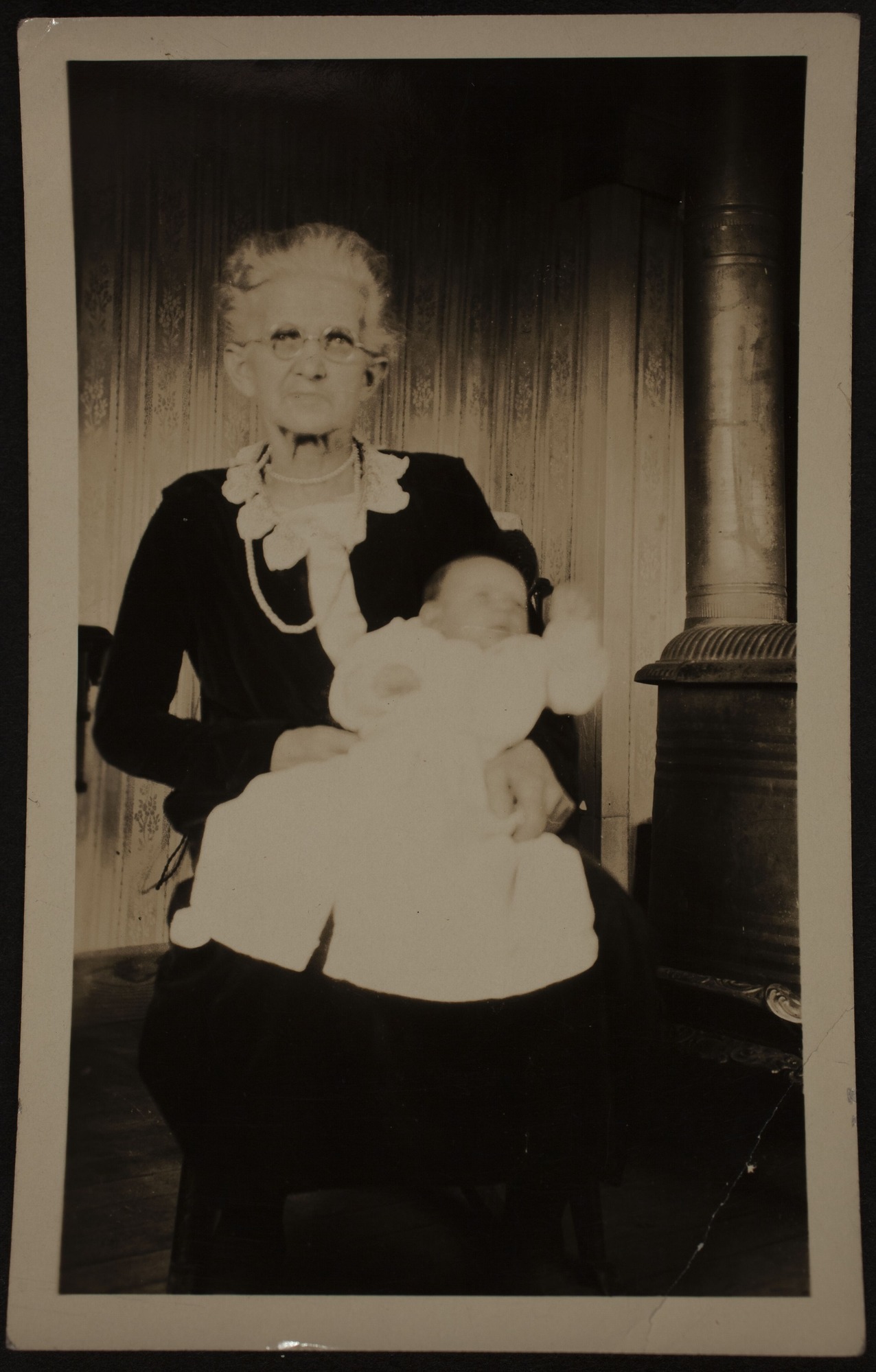 An elderly woman with white hair in a black dress holding a baby.