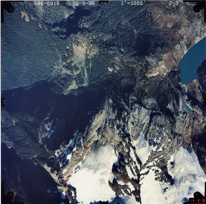 Color aerial photograph of glacier on mountain peak, surrounded by forested valleys.