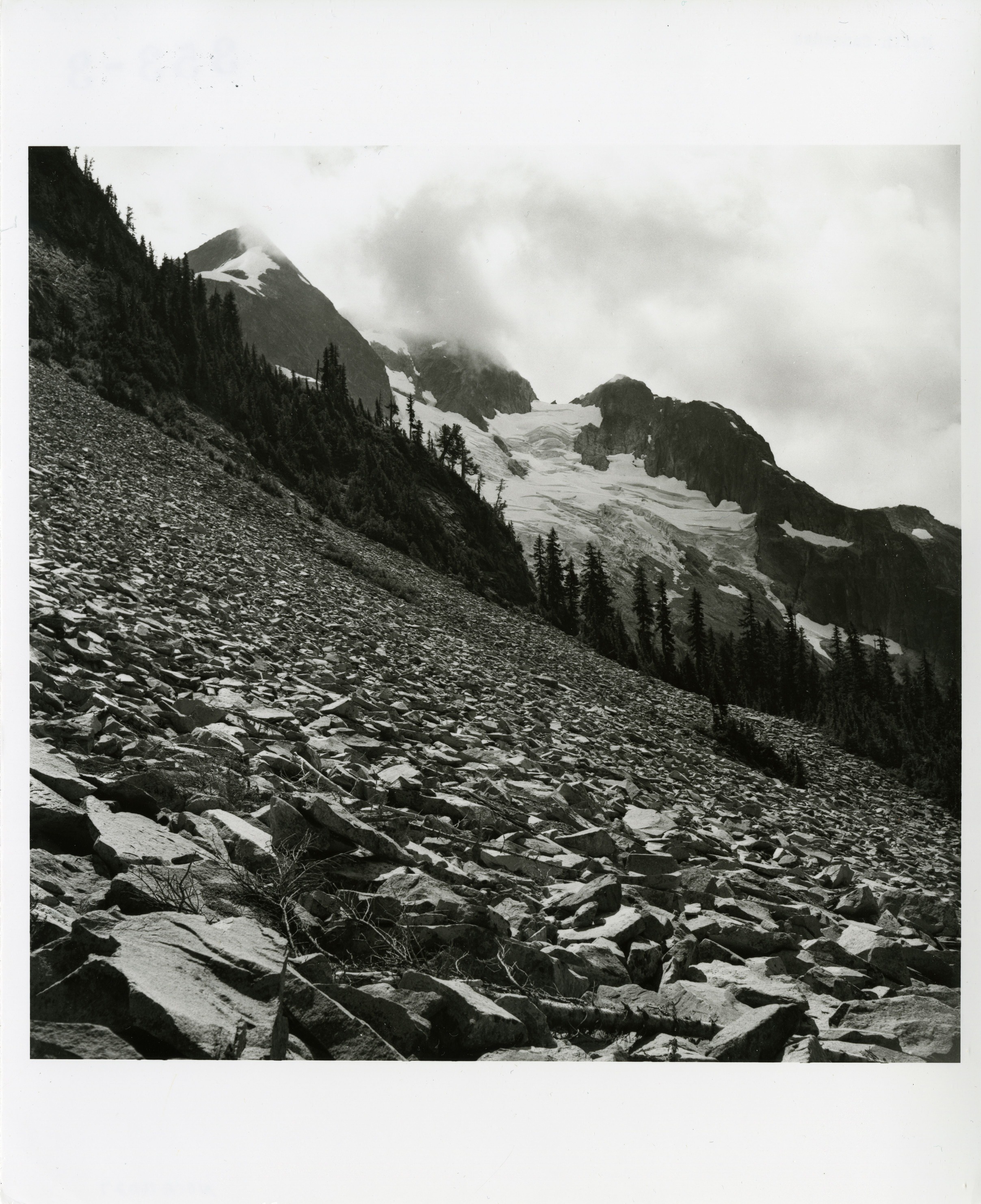 Talus covering the sides of a mountain. A mountain in the background is covered in a glacier.