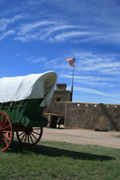 A green covered wagon parked outside next to a stone entry monument.