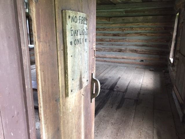 A wooden door in a log cabin with a sign on it.