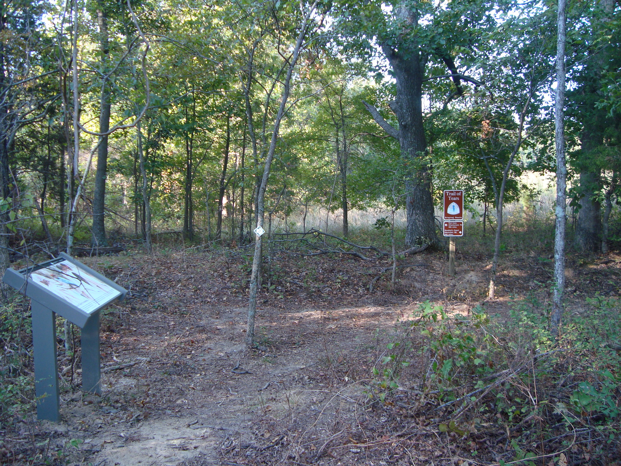 A sign and a wayside in the middle of a wooded area.