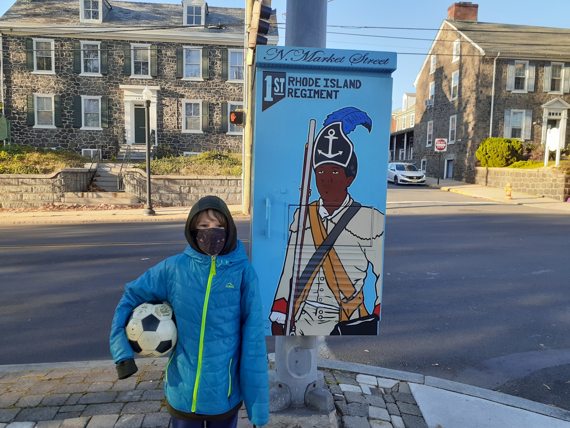Boy holding soccer ball next to graphics of 1st Rhode Island soldier. Location: Wilmington, DE