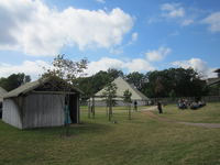 A group of people are sitting in a grassy area near a tepee.