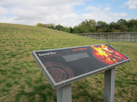 A wayside with some text and a picture on a grassy hill.