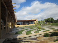 A wooden building with a green lawn and labyrinth garden under a partly cloudy sky.