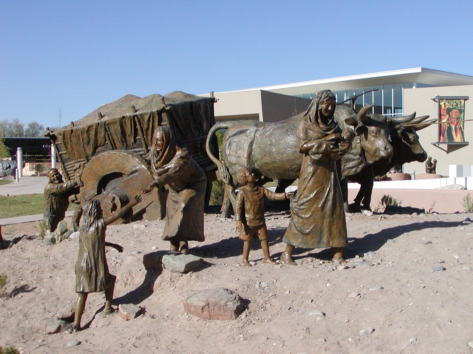 Women and children walk alongside the oxen and cart within the "La Jornada" statue at Albuquerque Museum Statue Garden.
