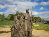 A statue under the open sky with some trees in the background.