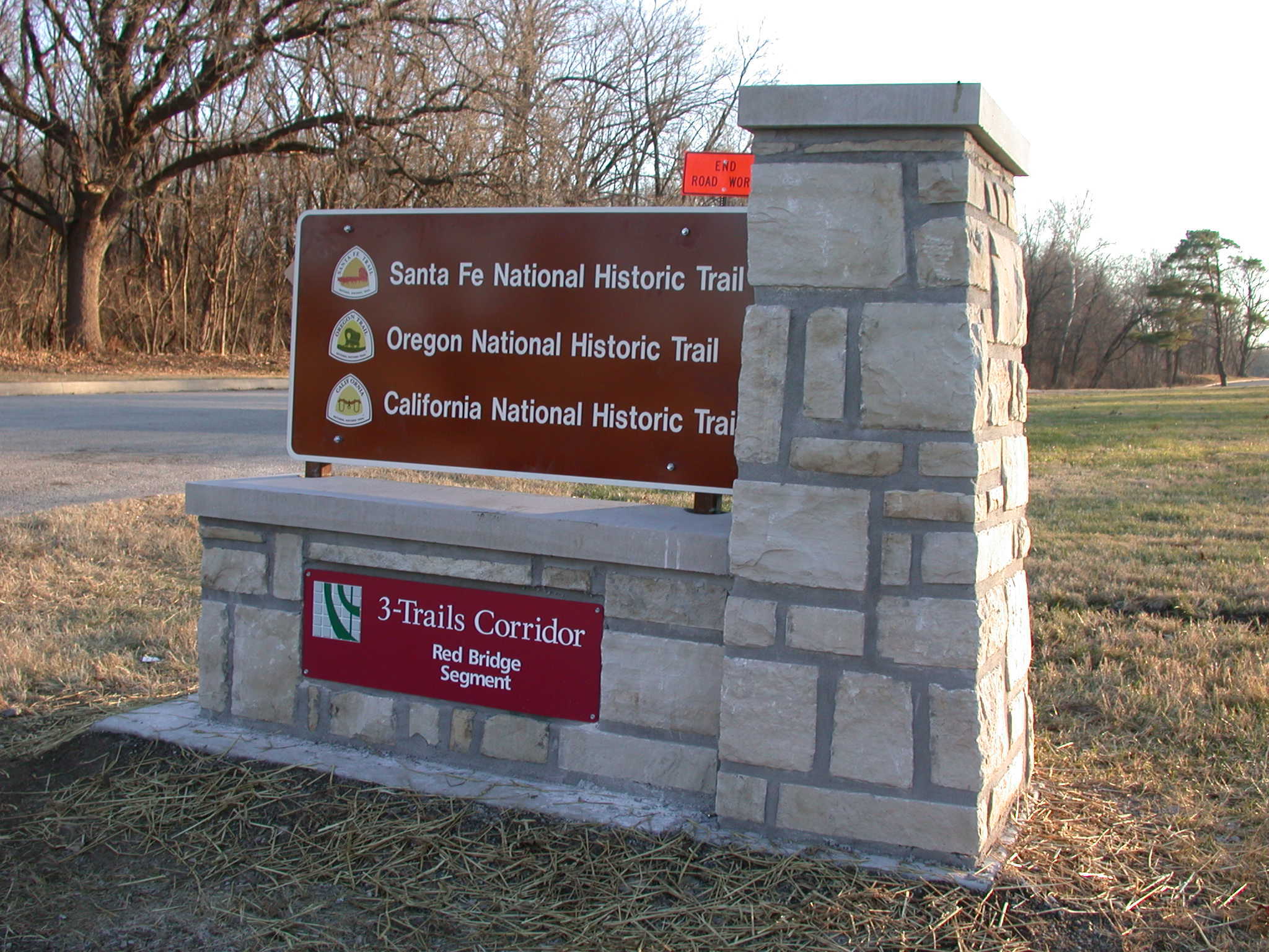 A signboard with the text "3 trails corridor" on it and a road in the background.