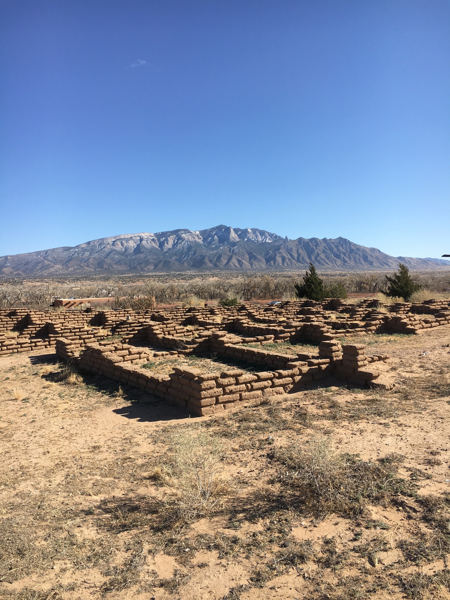 The ruins of an old adobe structure with mountains in the background.