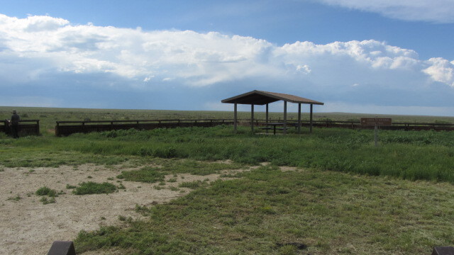 A shelter with a roof stands on a grassy field under a partly cloudy sky.