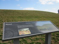 A wayside with some text and a picture on a grassy hill.