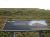 A wayside with some text and a picture on a grassy hill.