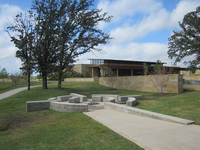 A park with benches, a walking path, trees, and a stone building under a cloudy sky.