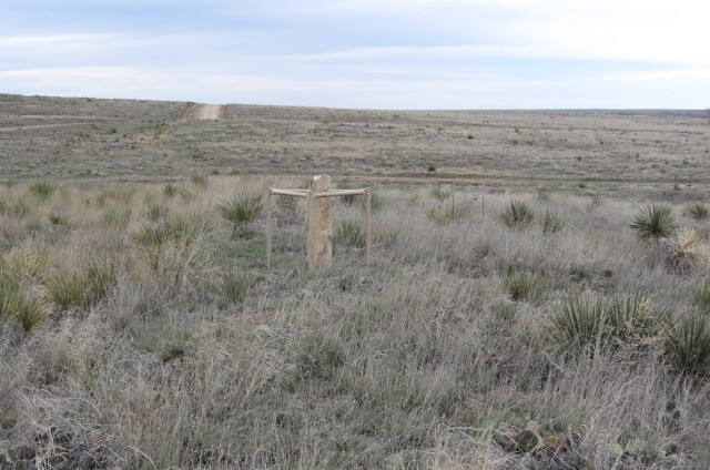 A grassy field with deep ruts and a marker on the prairie.