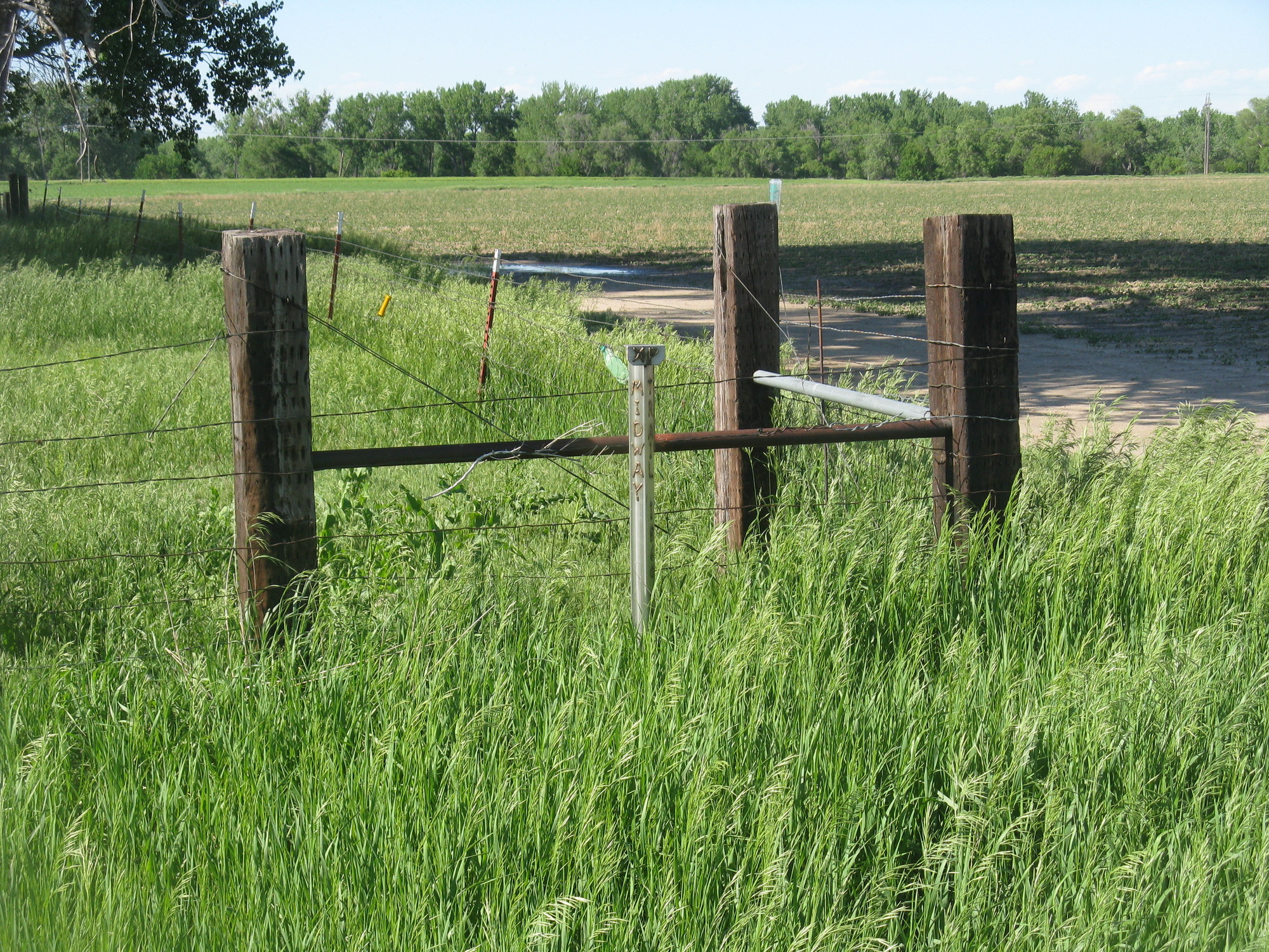 A metal pole sticking out of a grass field and surrounded by cropland marks the location of Midway Pony Express Station