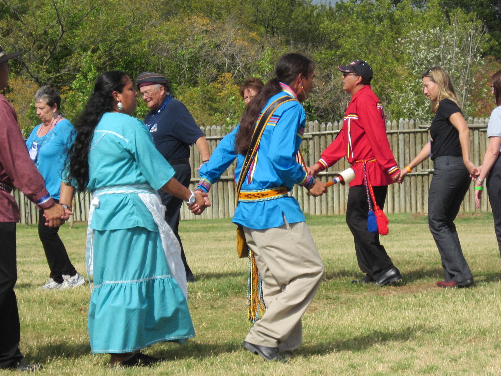 People holding hands and dancing in a circle on a grassy field outdoors.