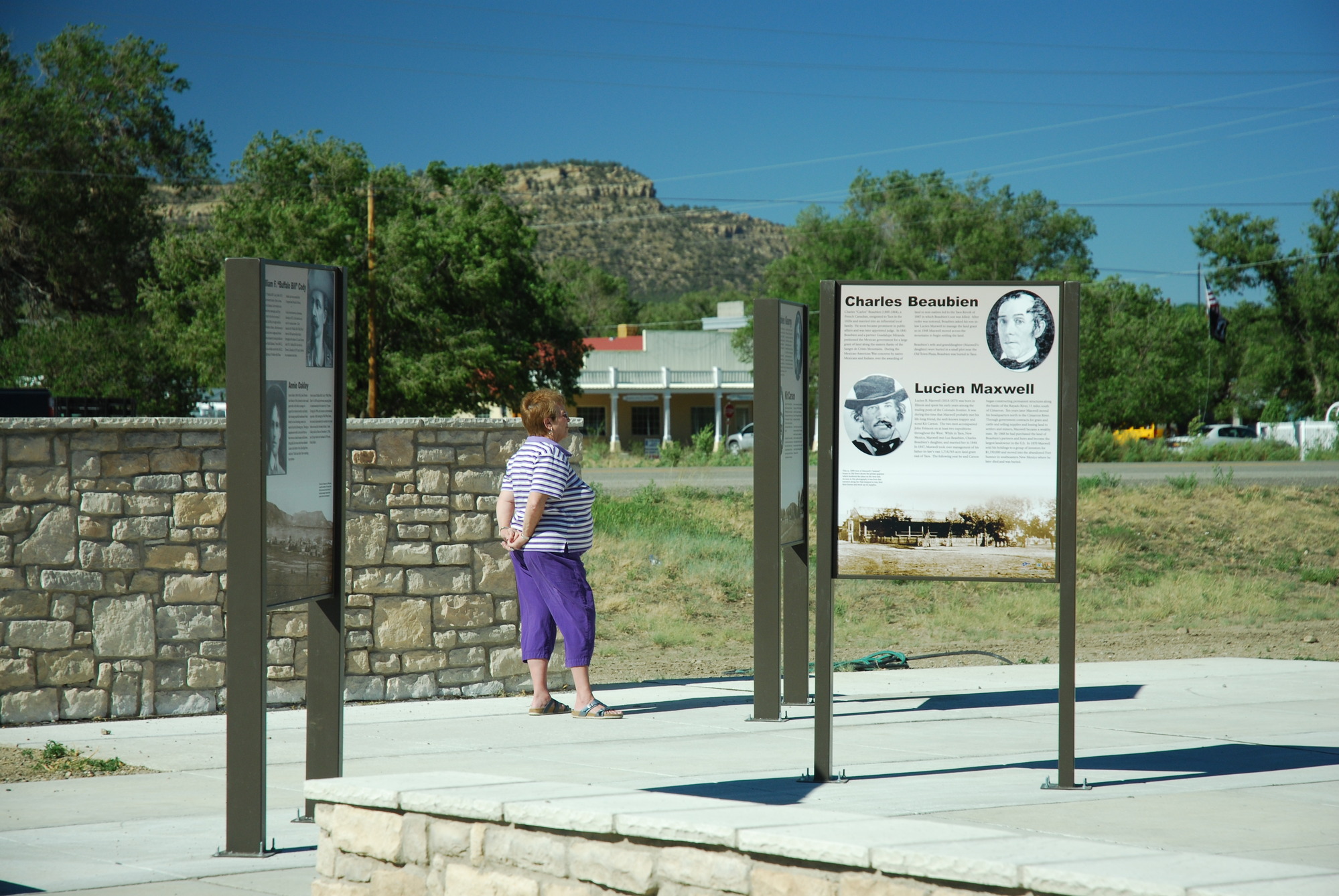 A woman is standing in front of a stone wall looking at a wayside.