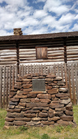 A stone wall with a sign in front of a log cabin.
