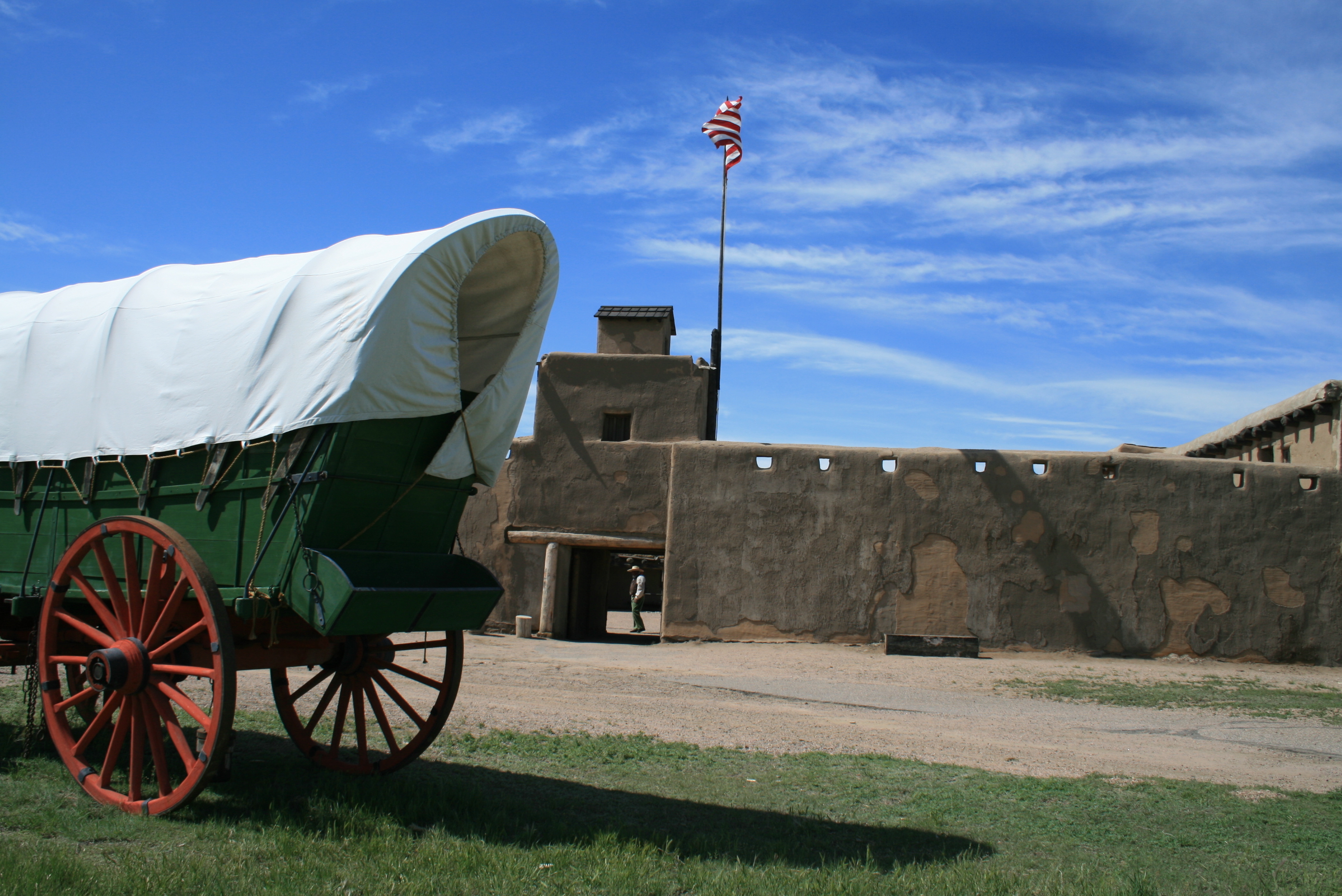 A green covered wagon parked outside next to a stone entry monument.