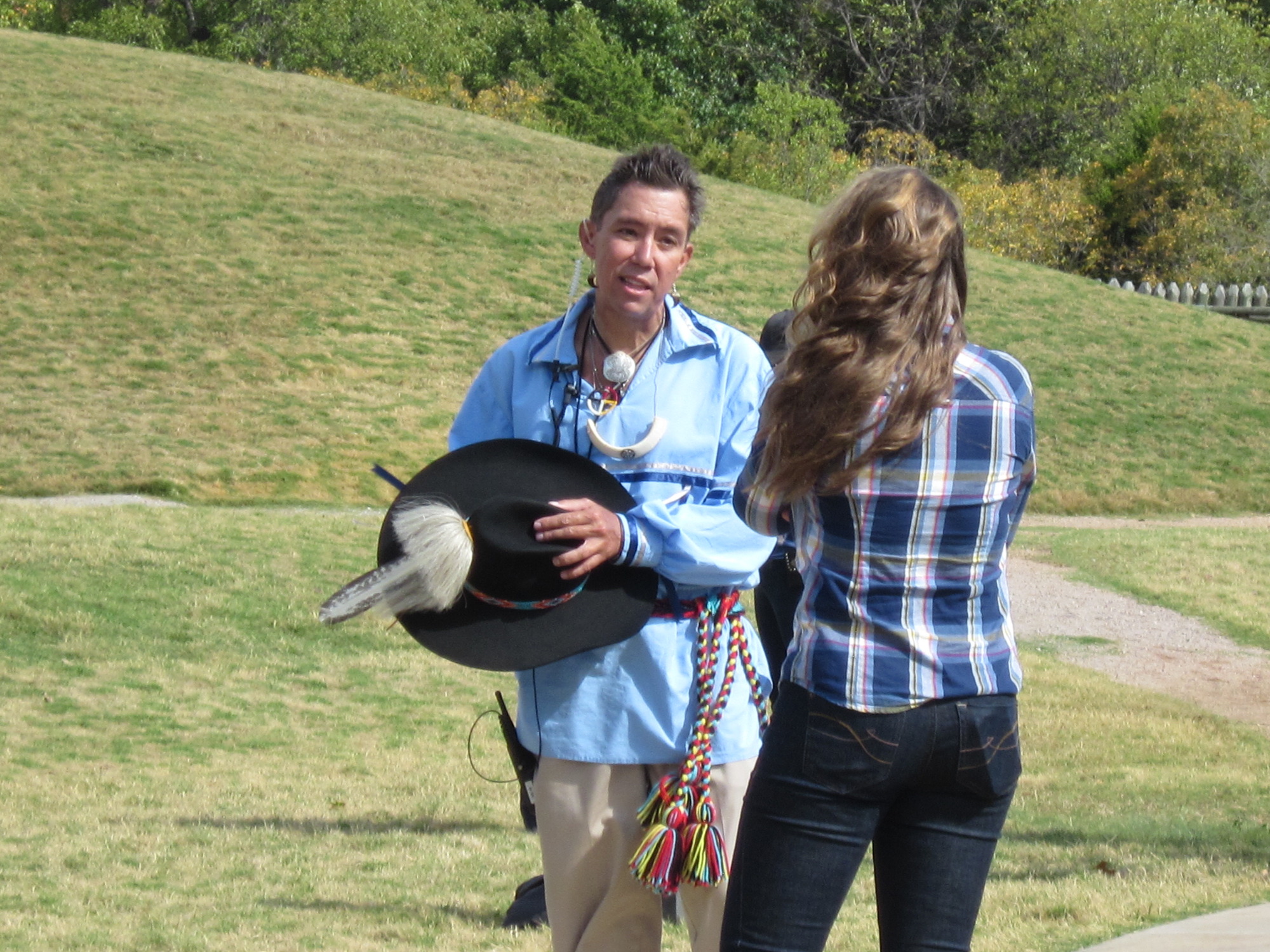 Two people holding a black hat and talking to each other in a grassy field.