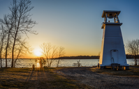 The sun sets over the Potomac river while a small white lighthouse stands at the water's edge as a sentinel and guide. 