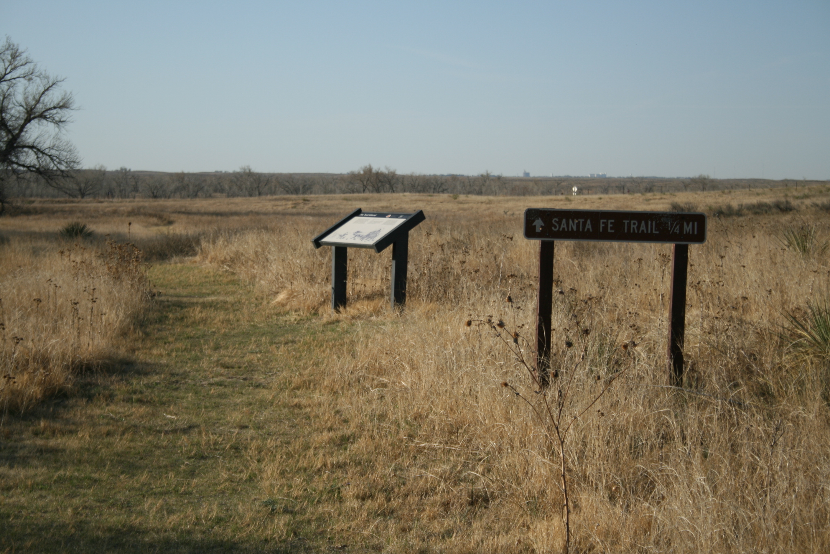 A trail sign reading "SANTA FE TRAIL 1/4 MI" next to awayside in a grassy field.
