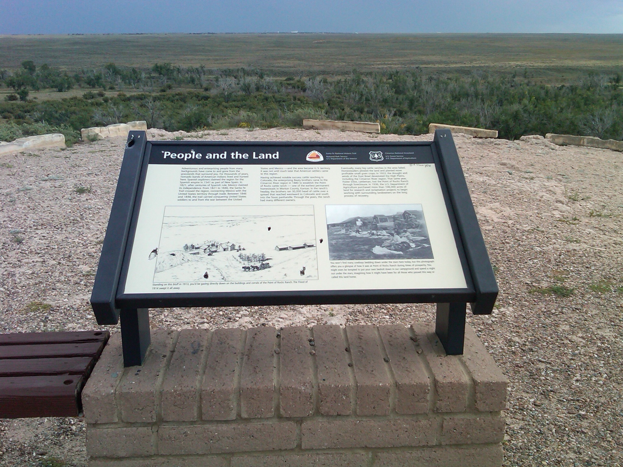 A wayside titled "People and the Land" with some text and illustration on it in a grassy field.