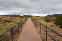 A metal railing on a path under the cloudy sky.