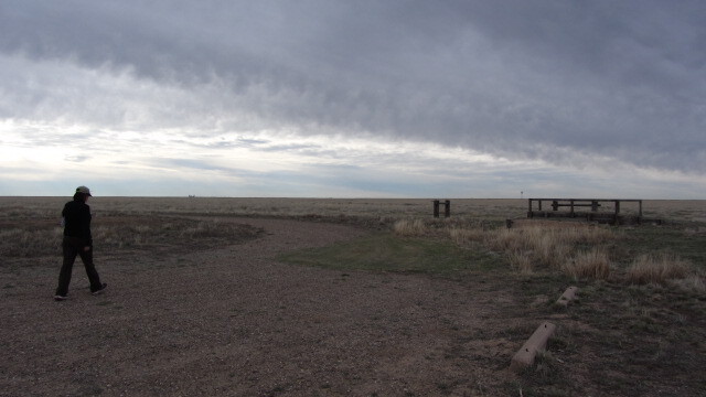 A man walking on a dirt road under a cloudy sky.
